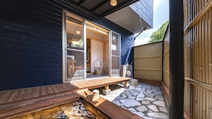 Een traditioneel Japans openlucht thermaalbad met een houten terras, stenen vloer en een houten omheining.