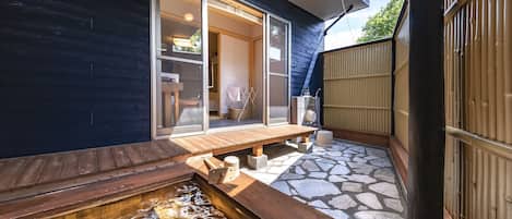 A traditional Japanese-style outdoor hot spring area with a wooden deck, stone flooring, and a wooden fence.
