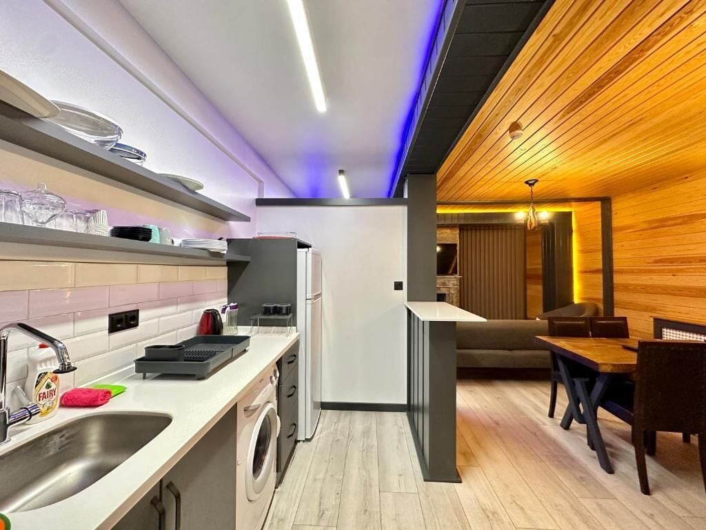 A modern kitchen with a washing machine, a dining area with a table and chairs, and a wooden accent wall.