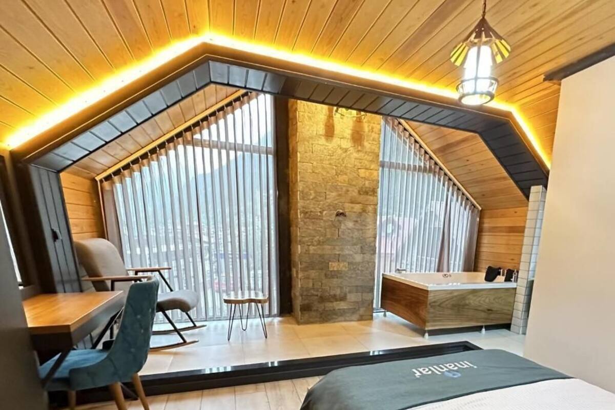 A modern bedroom with a sloped ceiling, a stone accent wall, a desk, and a bed.