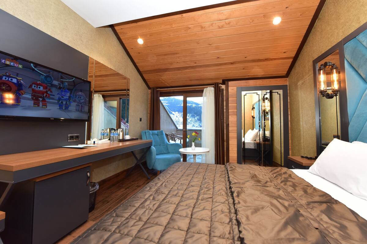 A hotel room with a bed, a desk, a chair, a TV, and a view of the mountains.