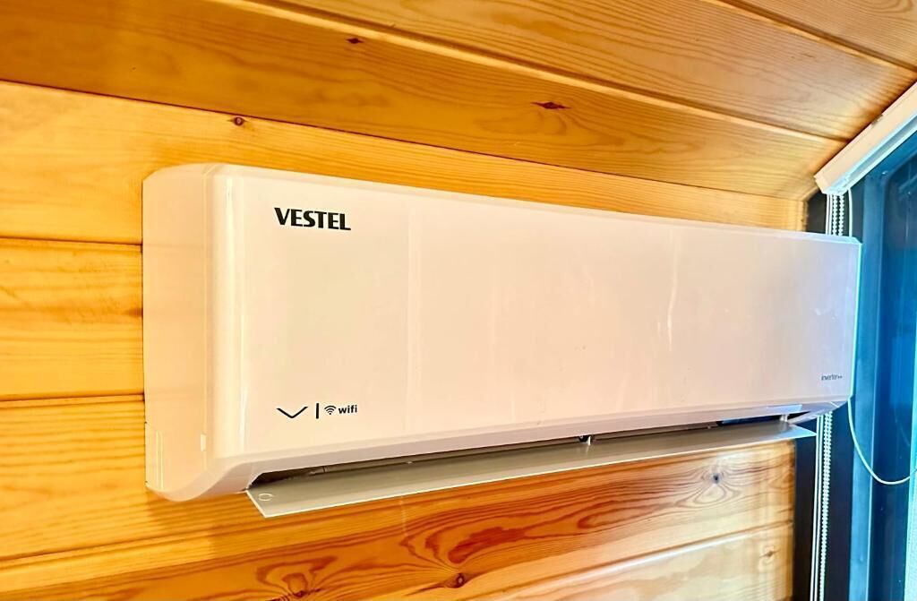 Un equipo de aire acondicionado VESTEL blanco montado en una pared de madera.