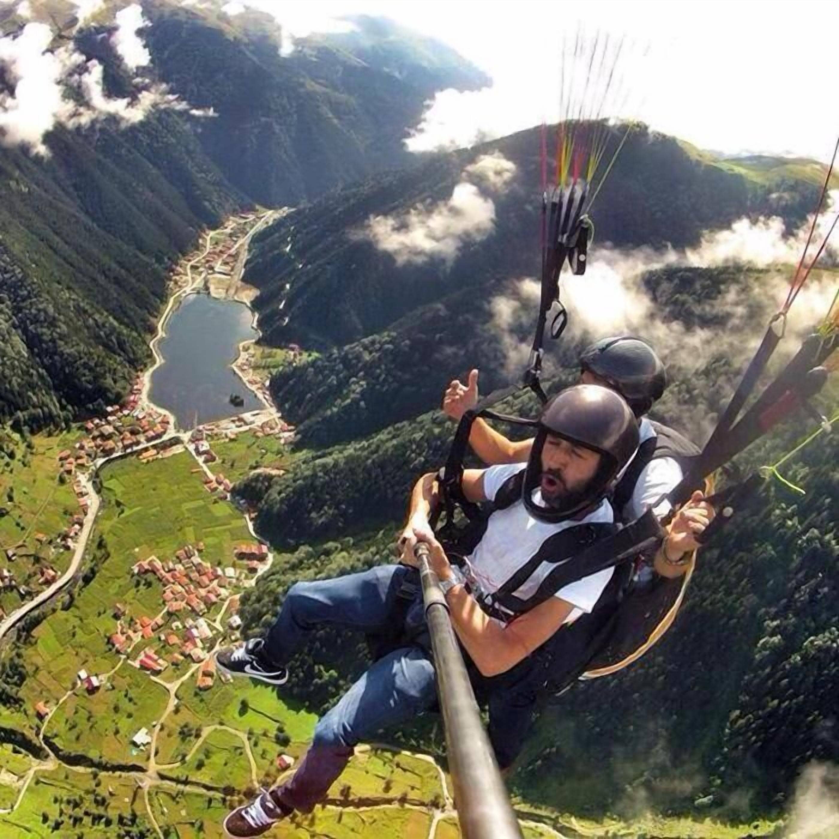 A person paragliding over a mountainous area with a lake and a village below.