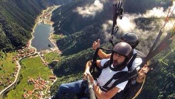 A person paragliding over a mountainous area with a lake and a village below.