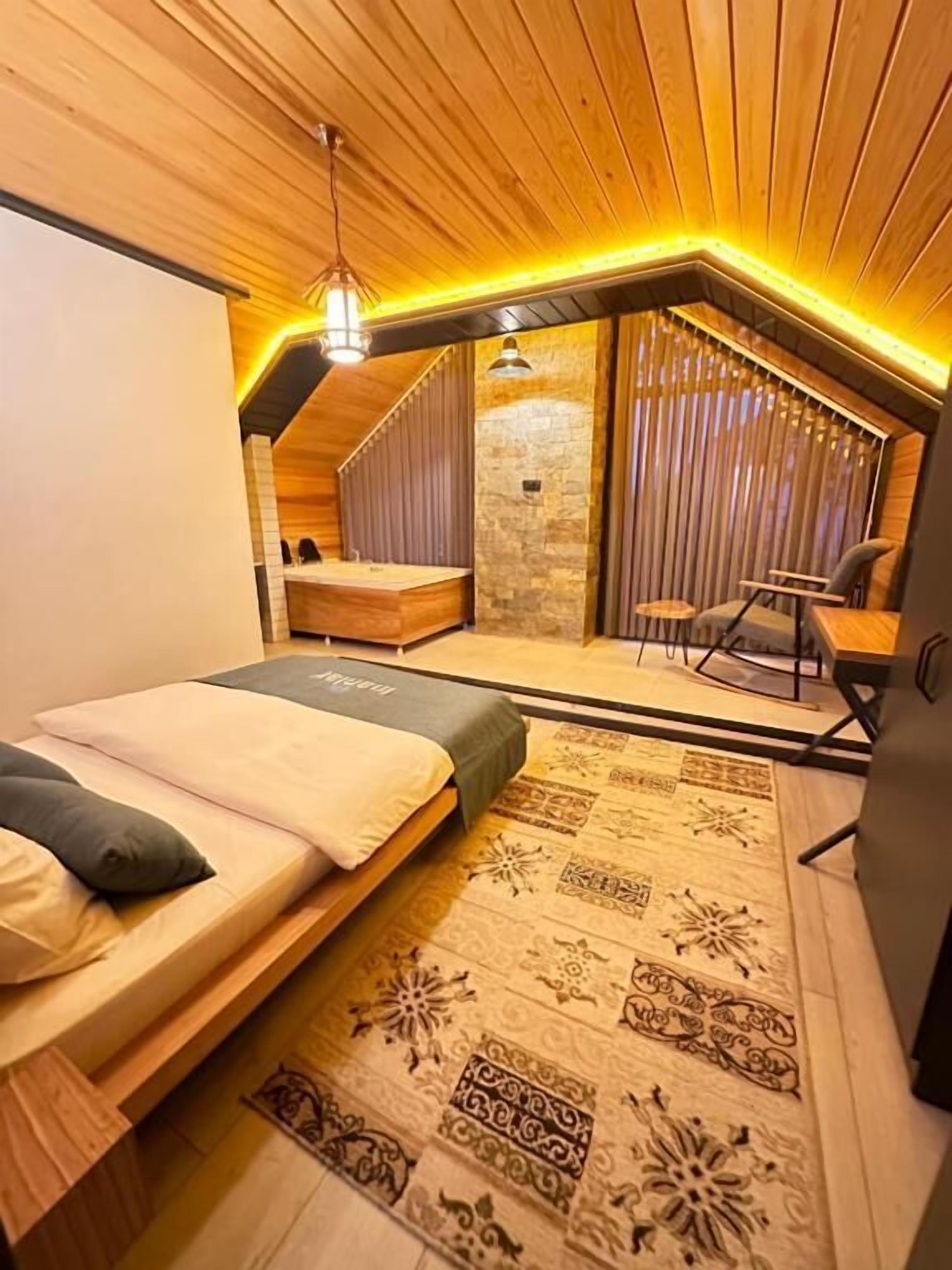 A cozy attic bedroom with a sloped ceiling, a bed with a patterned rug, a small seating area with a chair, and a stone accent wall.
