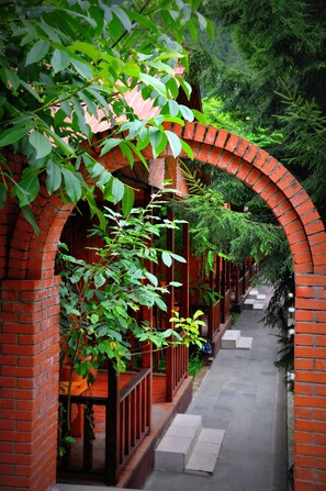 A narrow brick corridor with a wooden railing, surrounded by lush green foliage and a brick wall. - Inanlar Garden Hotel & Bungalow  (Çaykara)