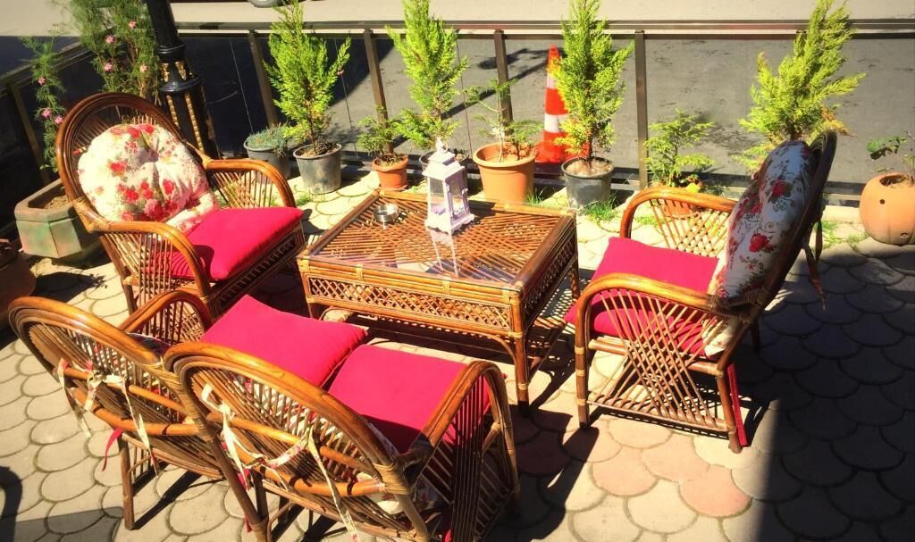 Mobilier en osier agrémenté de coussins rouges et une petite table ornée d’un objet décoratif, le tout placé sur une terrasse carrelée.