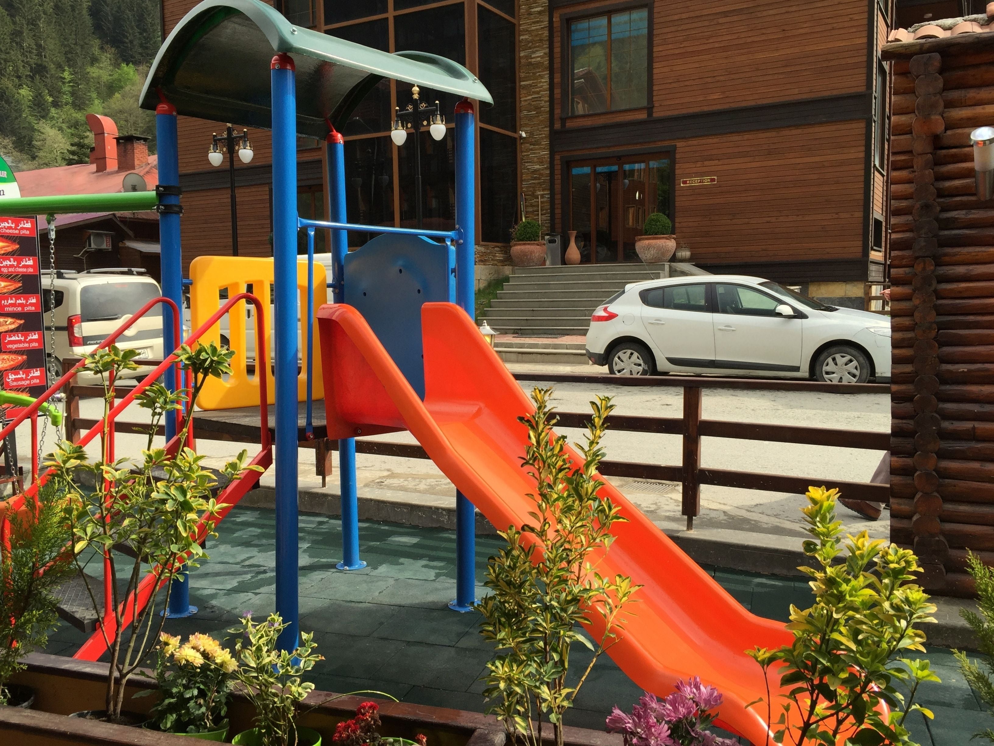 A playground with slides and climbing structures, a reception area, and a building with a wooden facade.