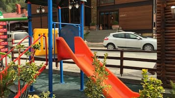 A playground with slides and climbing structures, a reception area, and a building with a wooden facade.