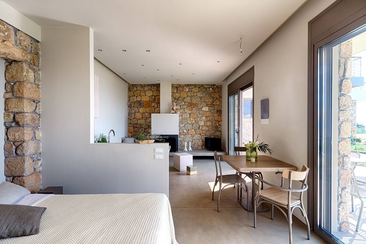 Une chambre d’hôtel moderne avec un mur en pierre, un lit, un coin repas avec des chaises et un téléviseur.