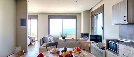 A modern kitchen with a dining area, large windows, and a view of the ocean.