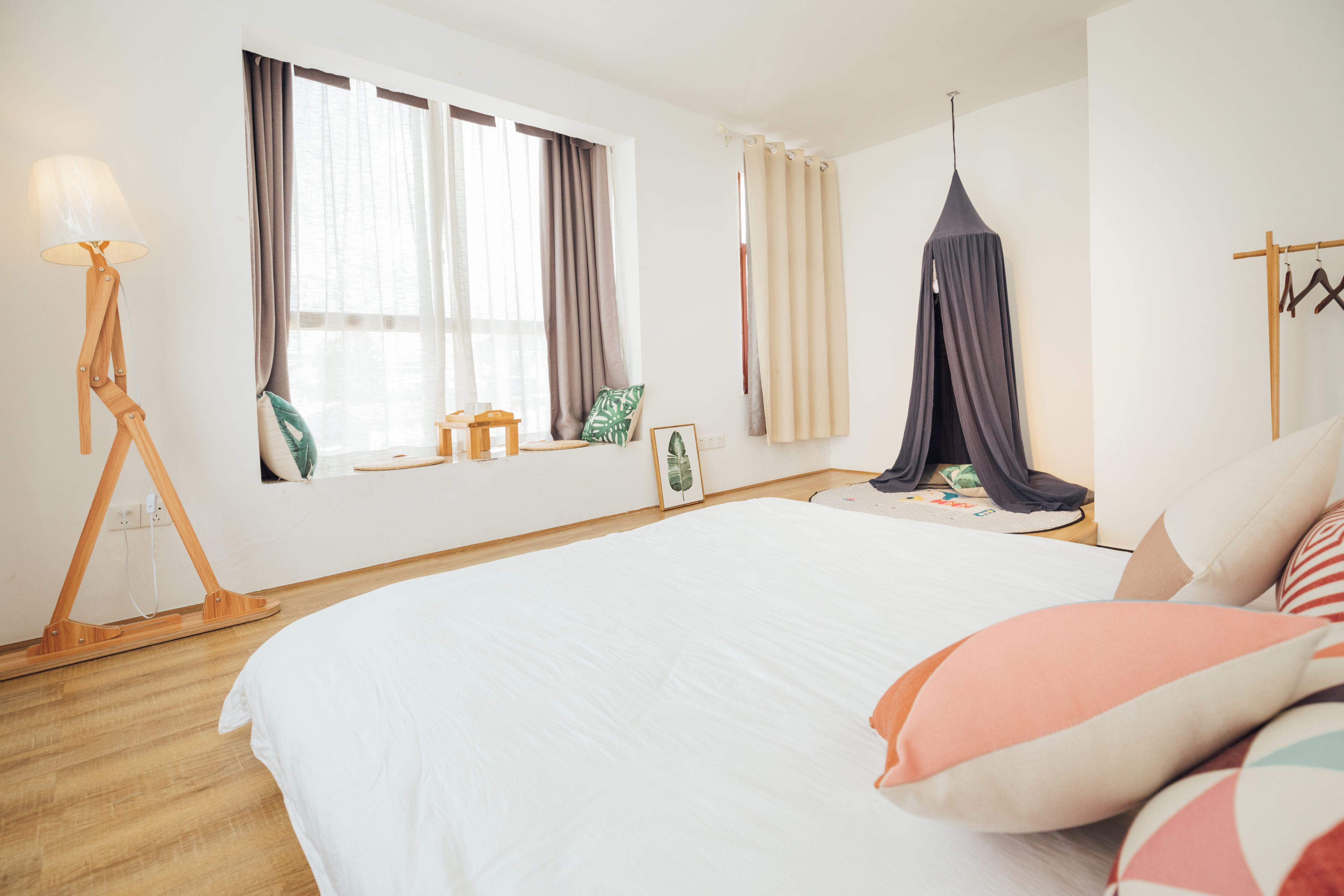 A bedroom with a large bed, a bedside table, a lamp, a window with curtains, and a hanging canopy.