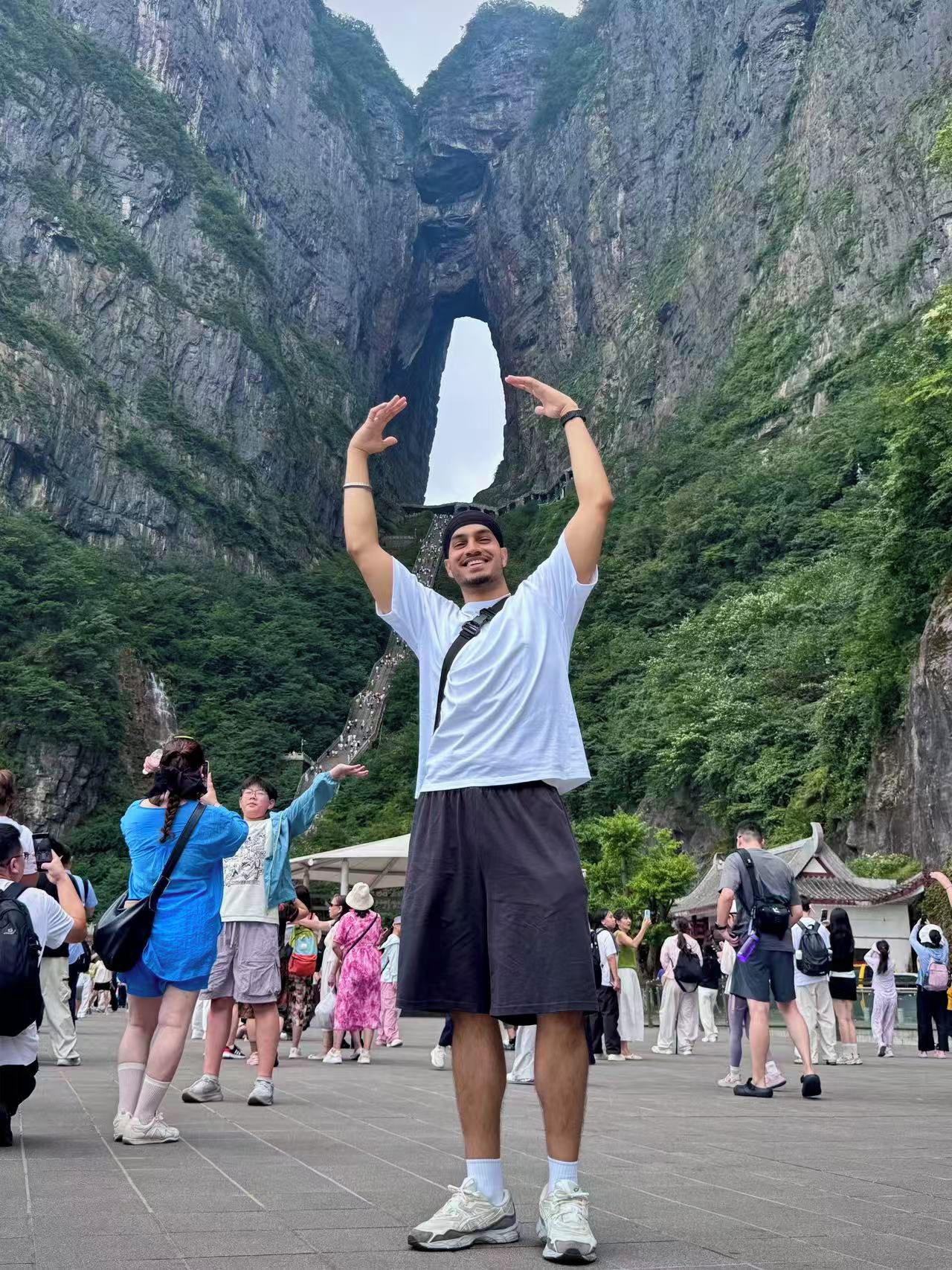 A person standing in a plaza with a mountainous backdrop, surrounded by other visitors.