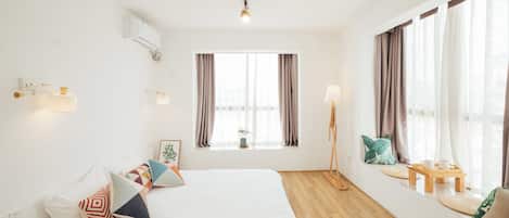 A hotel room with a bed, a desk, a standing lamp, and a window with curtains.