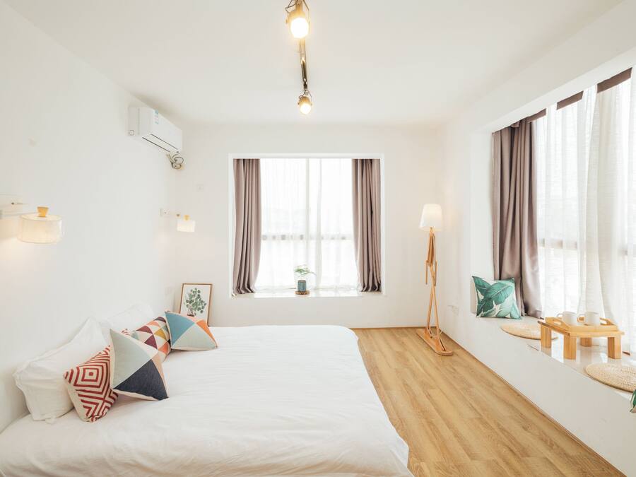 Una habitación de hotel con cama, escritorio, lámpara de pie y ventana con cortinas.