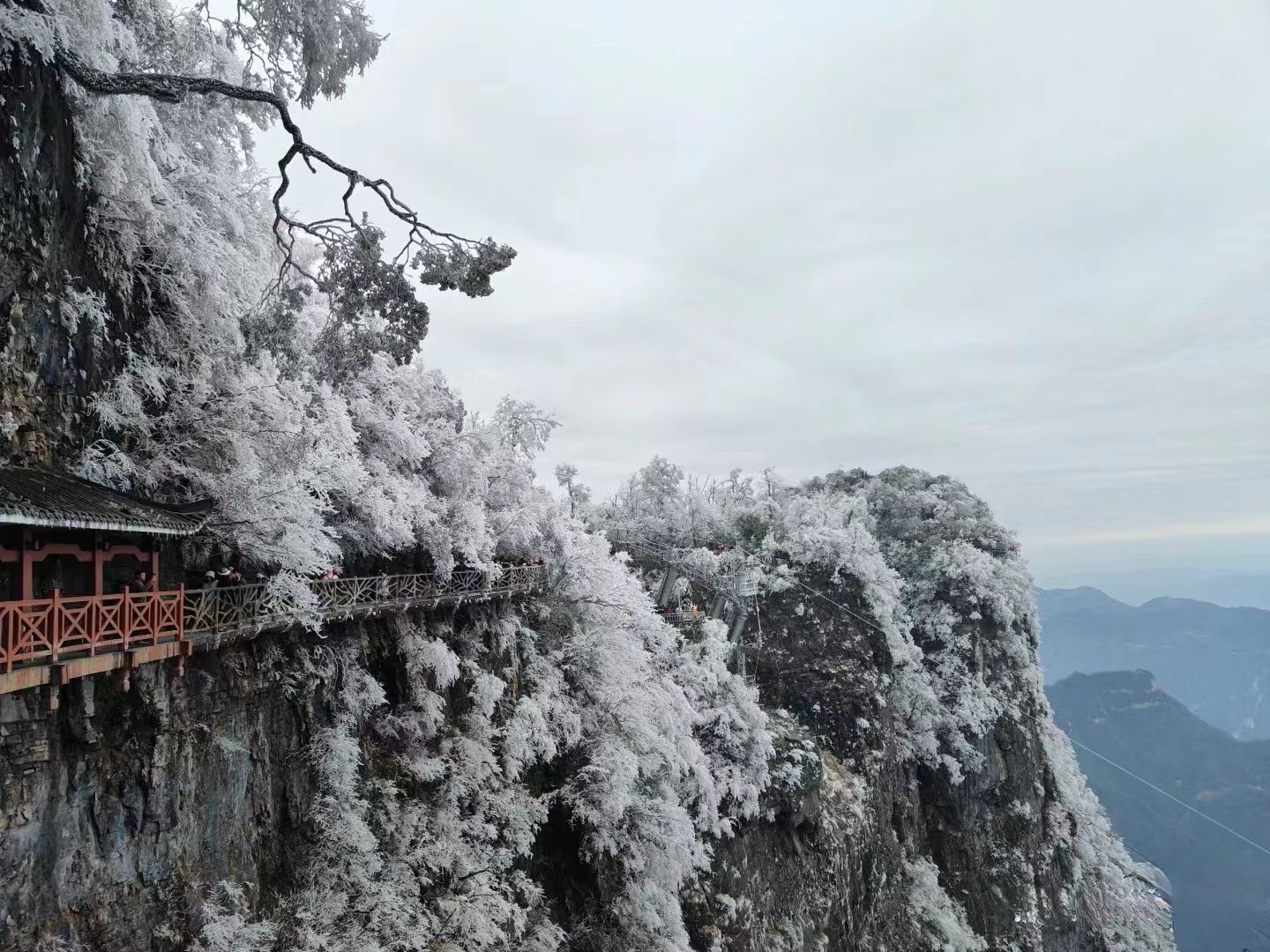 A traditional building with a red roof and a wooden walkway on a cliffside.