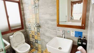 A bathroom with a toilet, shower, sink, and a mirror.
