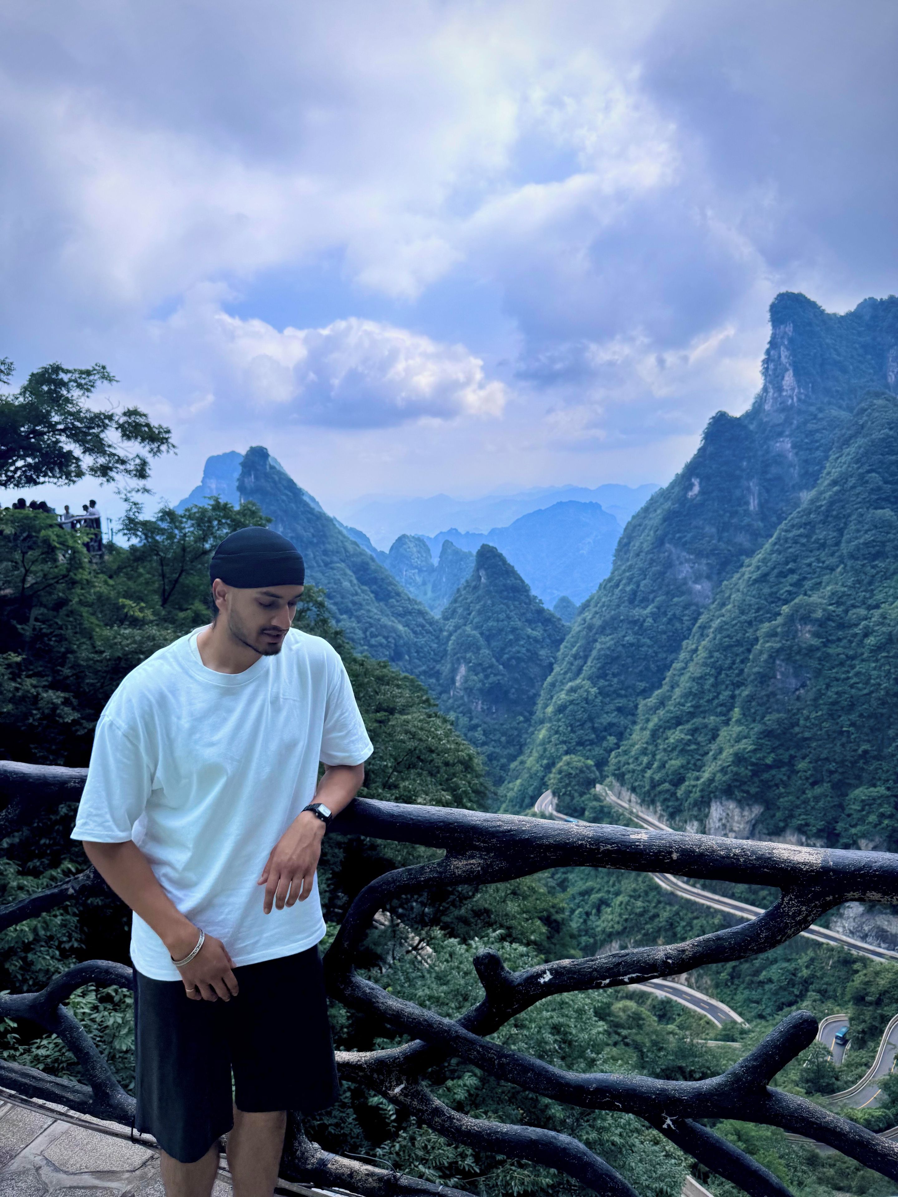 A person standing on a balcony overlooking a mountainous landscape with a winding road.