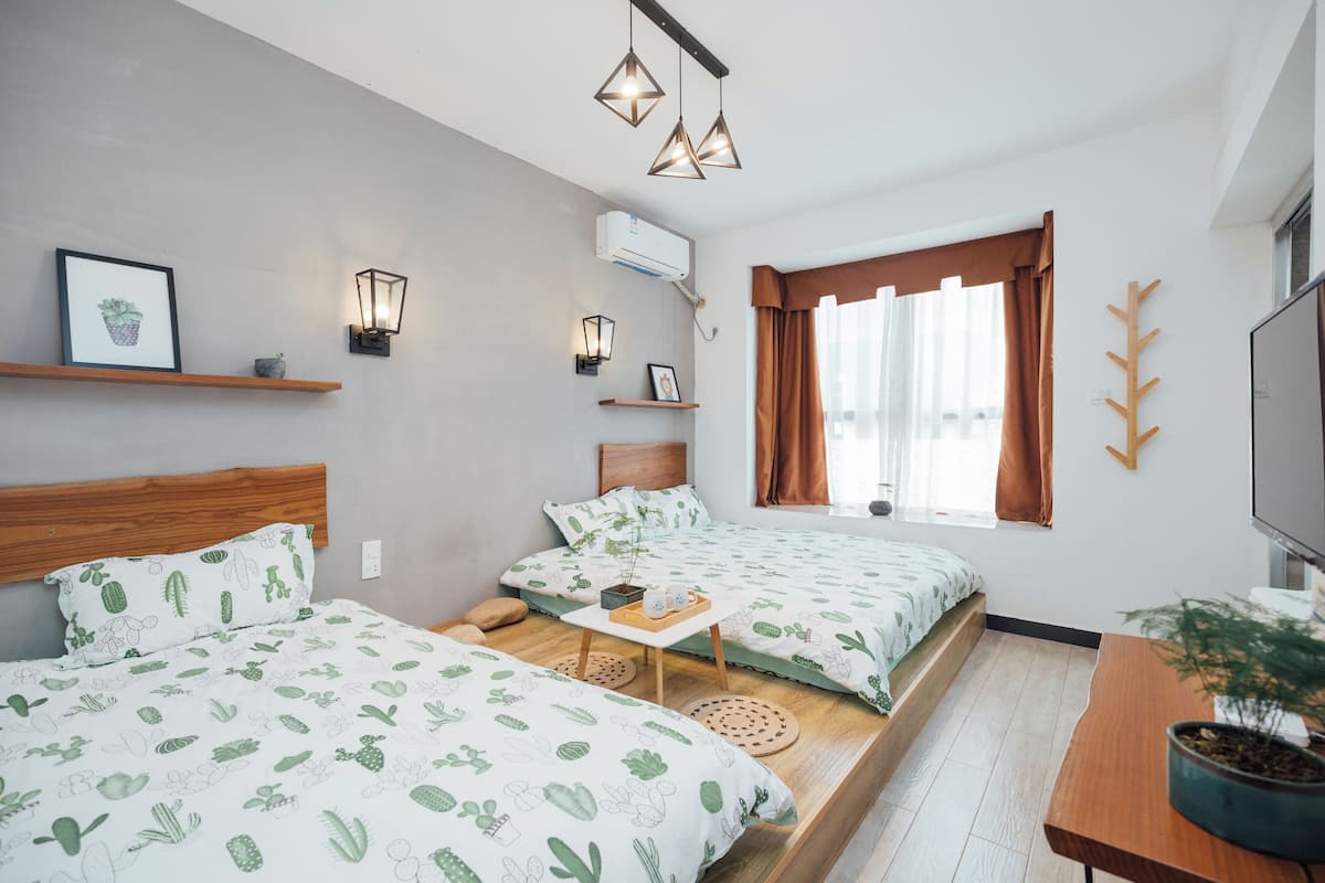 A modern bedroom with two beds, a small table, a TV, and a window with curtains.