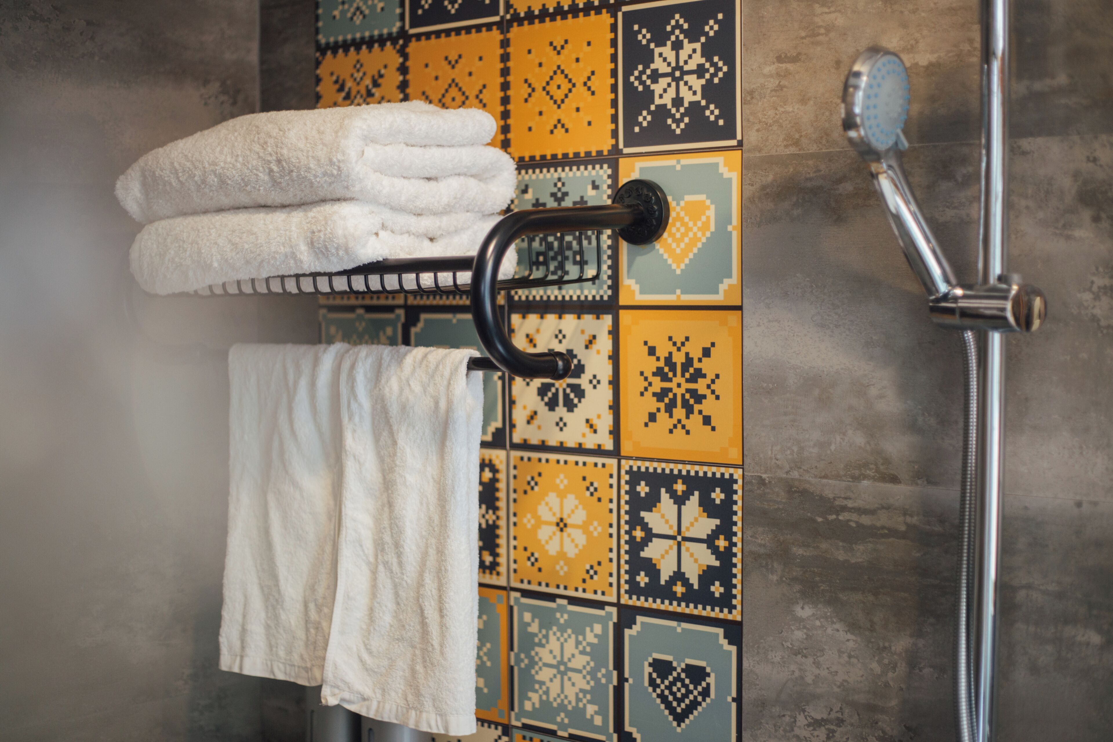 A bathroom with a tiled wall, a towel rack with folded towels, and a showerhead.