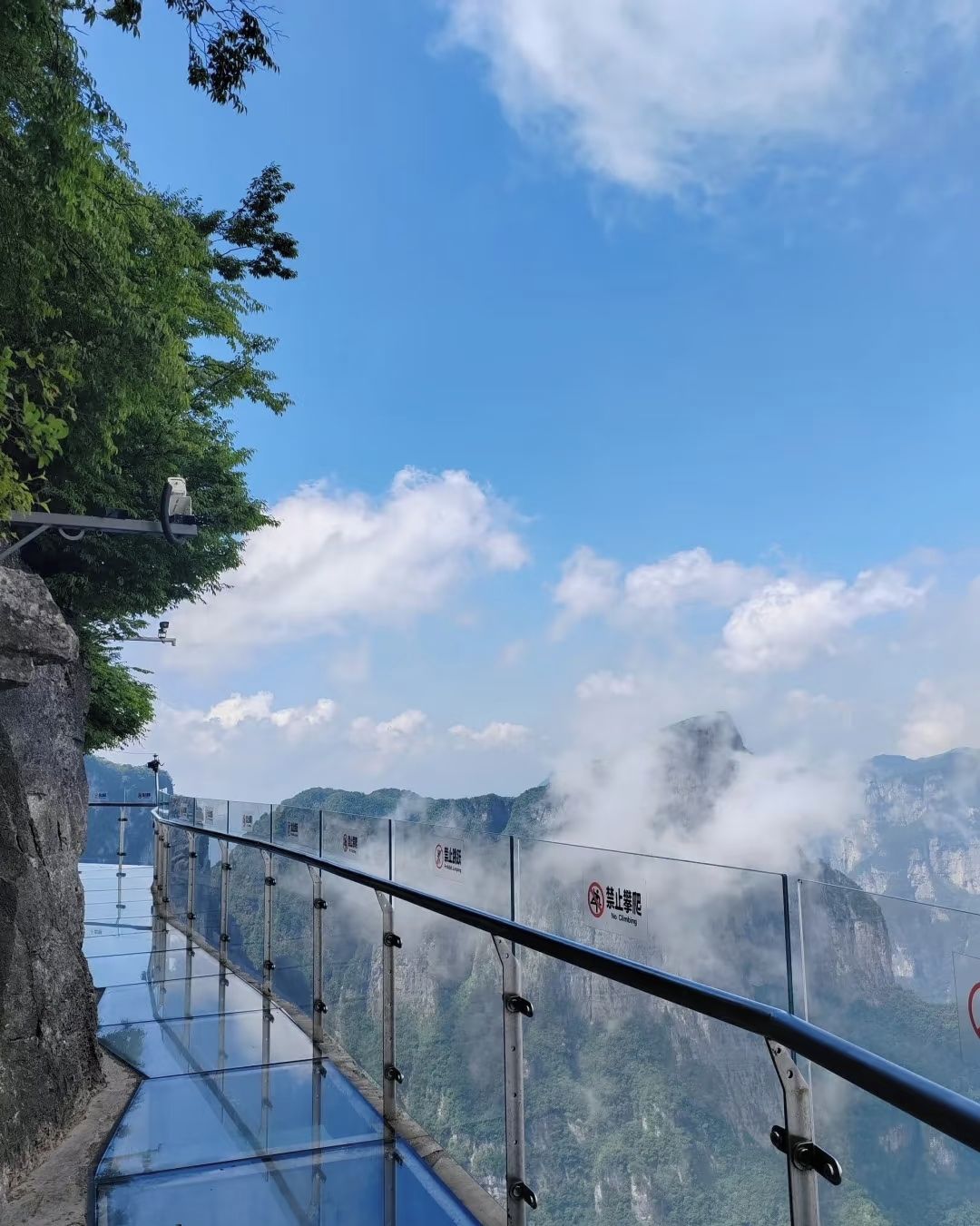 A glass bridge with railings, overlooking a mountainous landscape with clouds.