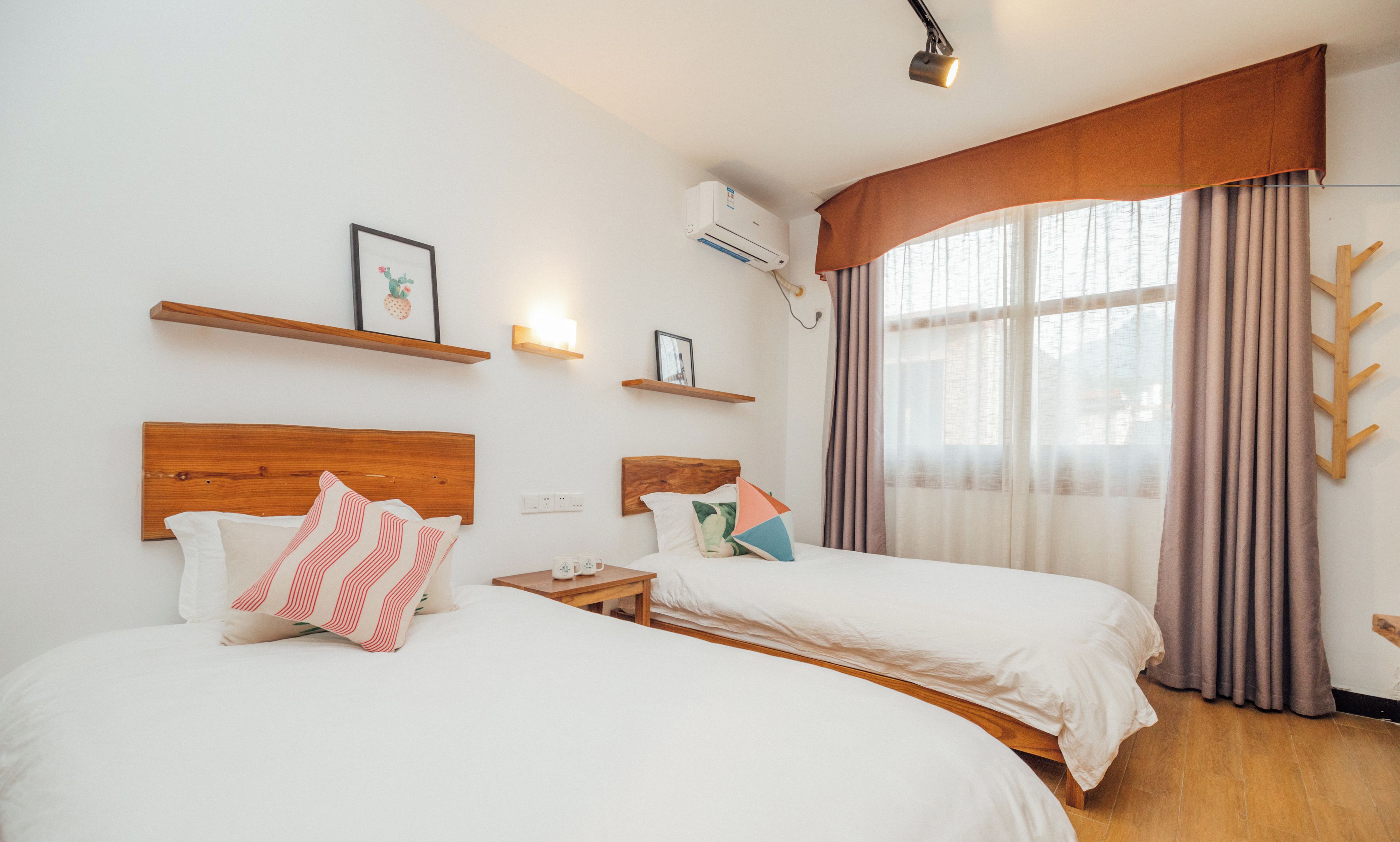 A hotel room with two beds, a wooden headboard, a wall-mounted air conditioner, and a window with curtains.