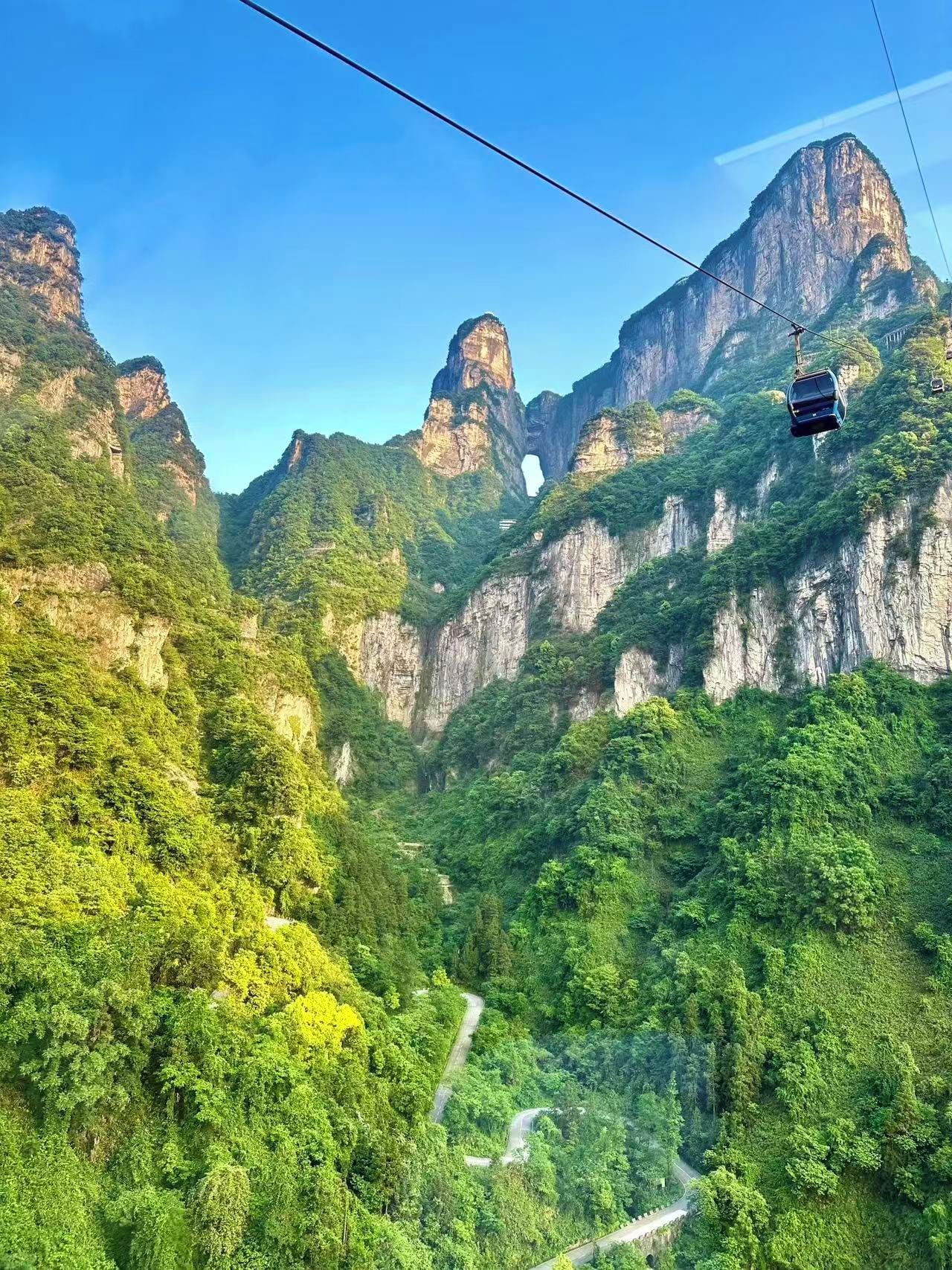 A cable car system in a mountainous area with lush greenery and rocky cliffs.