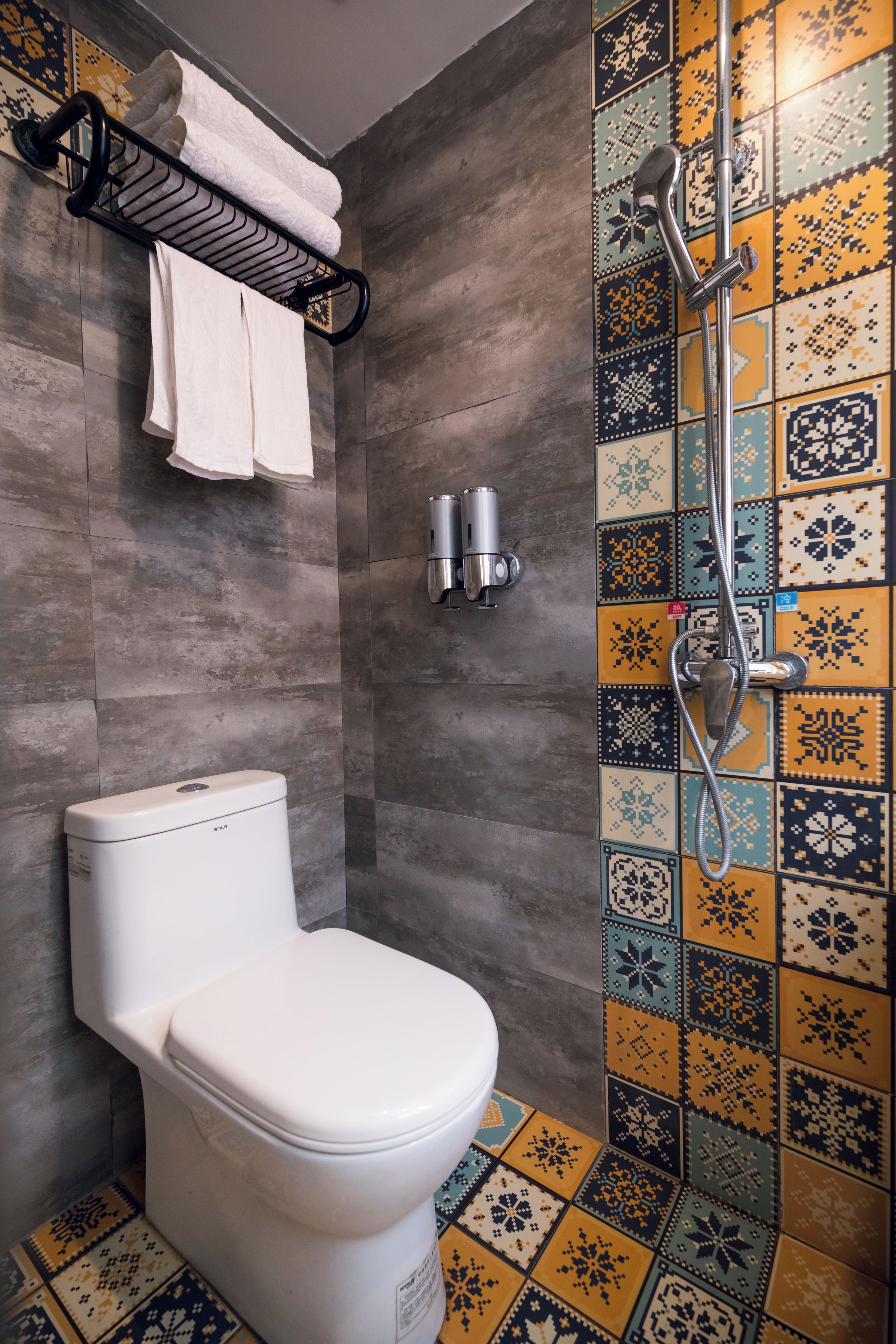 A bathroom with a toilet, a towel rack with towels, a shower, and a tiled wall.