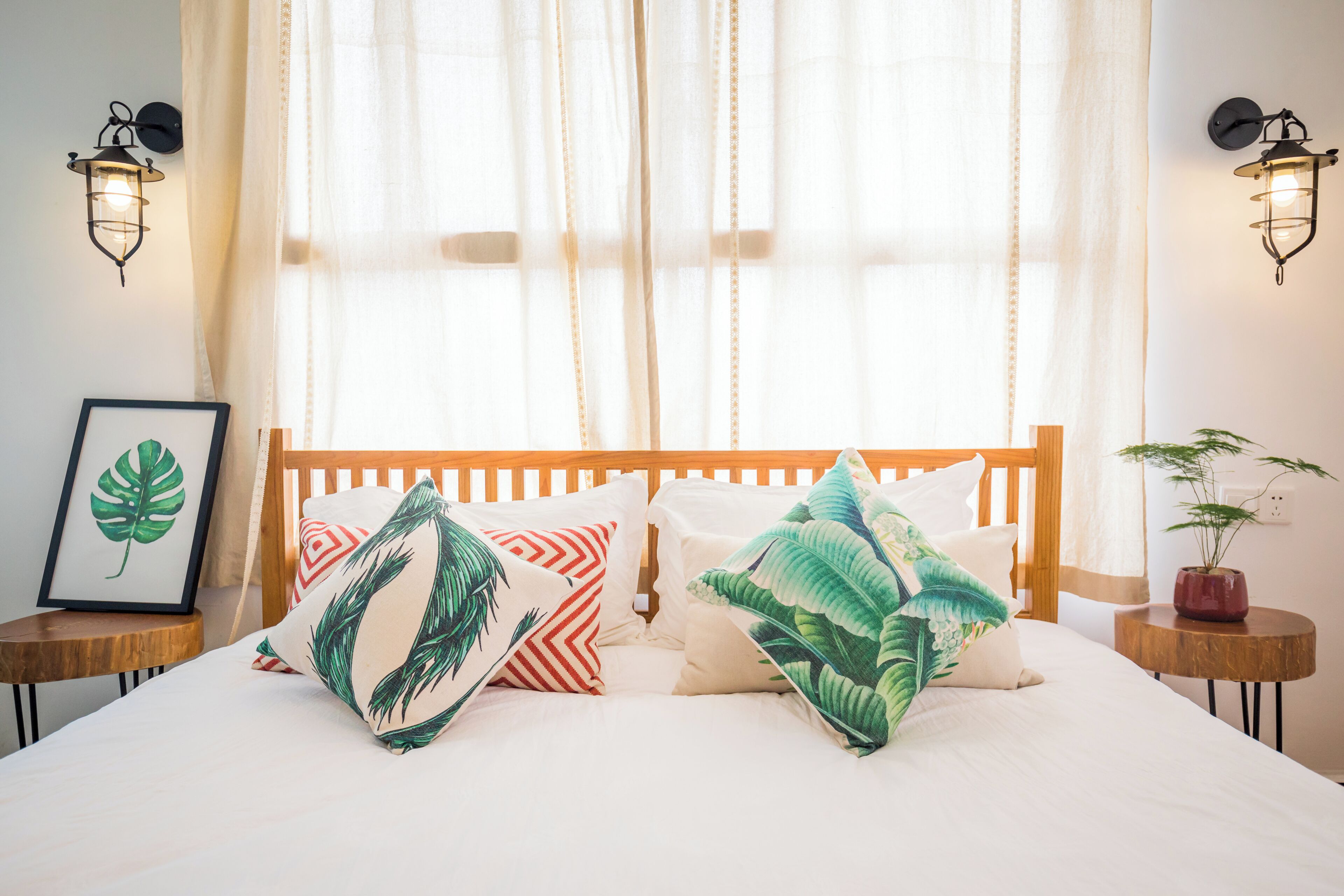 Ein Bett mit Holz-Kopfteil, zwei Wandleuchten, einem gerahmten Bild und einem Blumentopf.