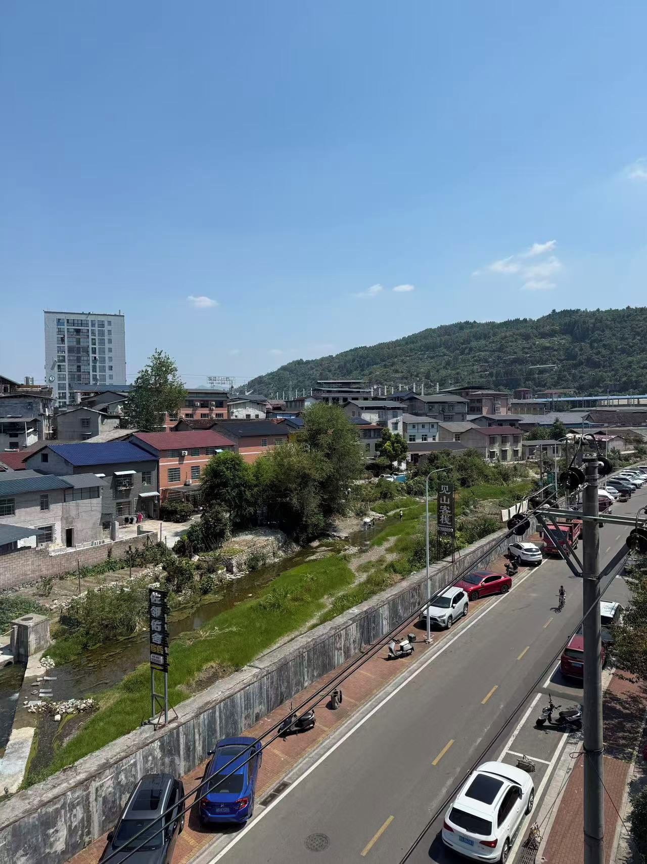 A multi-story building with a flat roof, surrounded by smaller buildings and a hilly landscape.