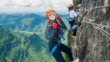 Una persona haciendo rappel por un risco, con una vista panorámica de un valle boscoso abajo.