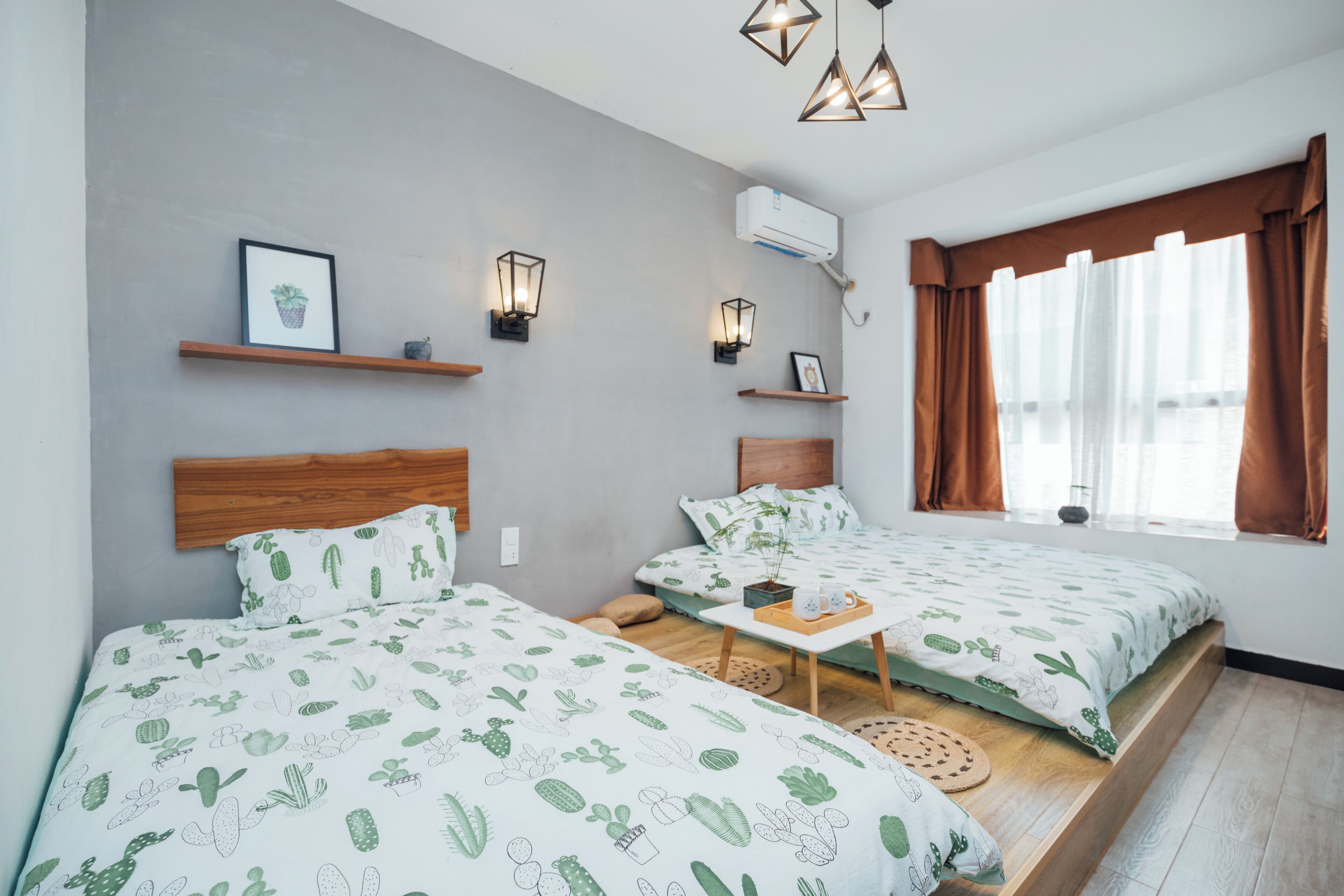 Una habitación con dos camas, una mesita, luces en la pared y un ventanal con cortinas.