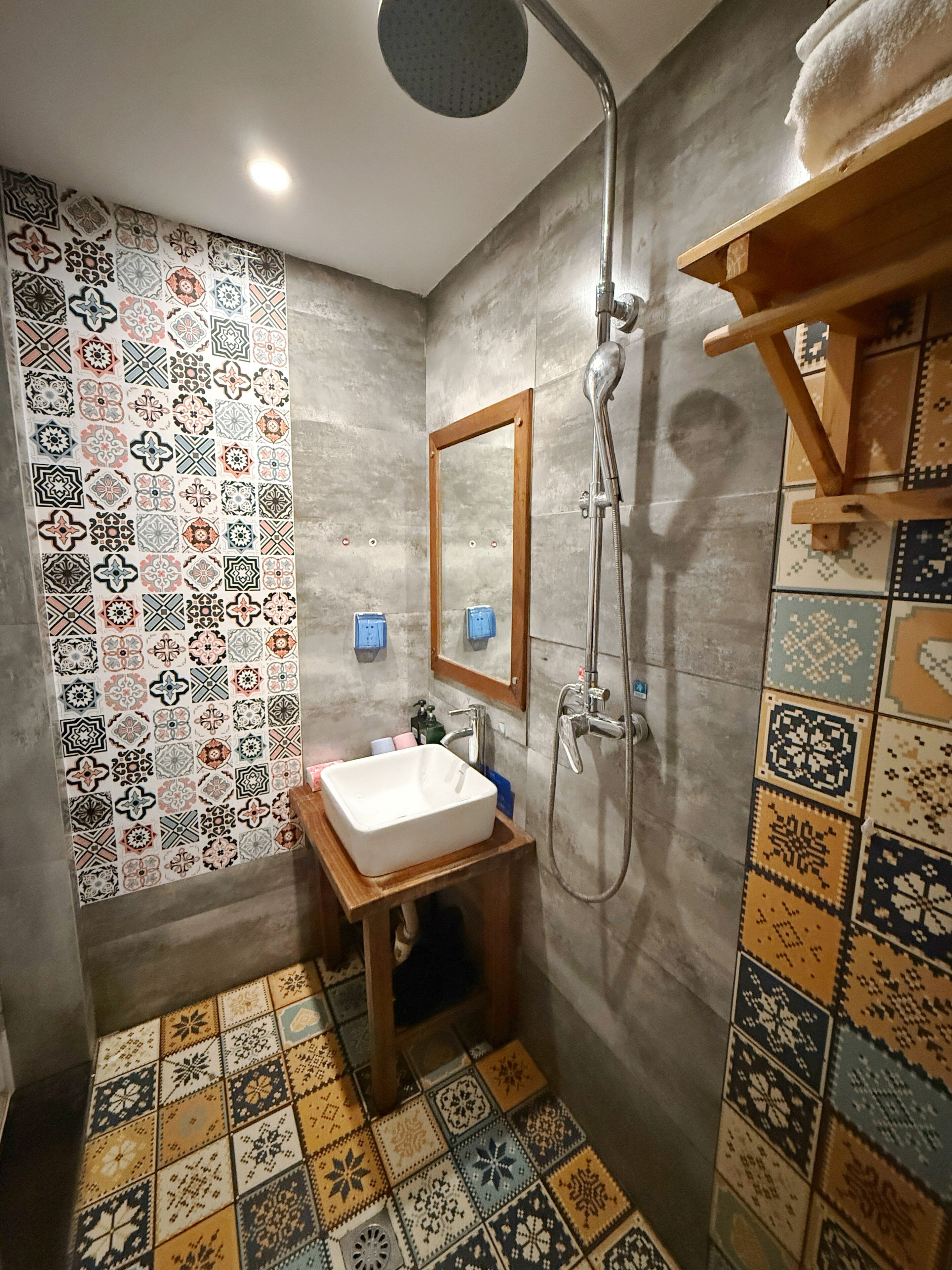 A bathroom with a sink, mirror, shower, and patterned tiles.