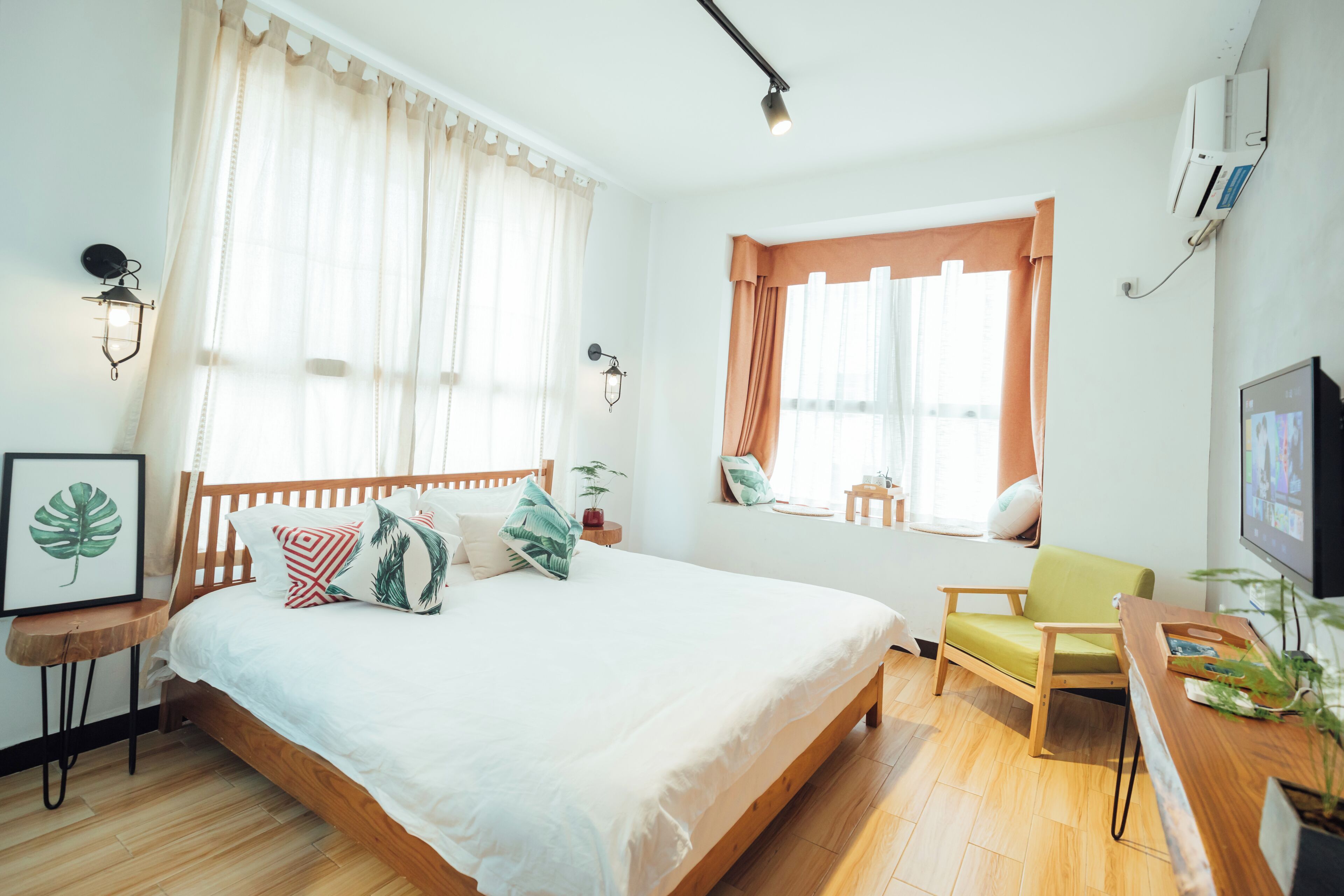 A bedroom with a bed, a desk, a chair, a window with curtains, wall-mounted lights, and a framed picture.