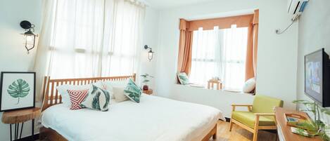 A bedroom with a bed, a desk, a chair, a window with curtains, wall-mounted lights, and a framed picture.