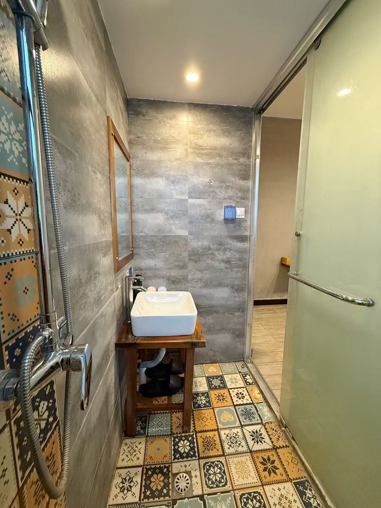 A bathroom with a shower, a sink, a mirror, and patterned floor tiles.