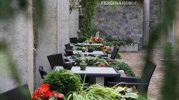 An outdoor dining area with wicker tables and chairs, surrounded by potted plants and flowers.