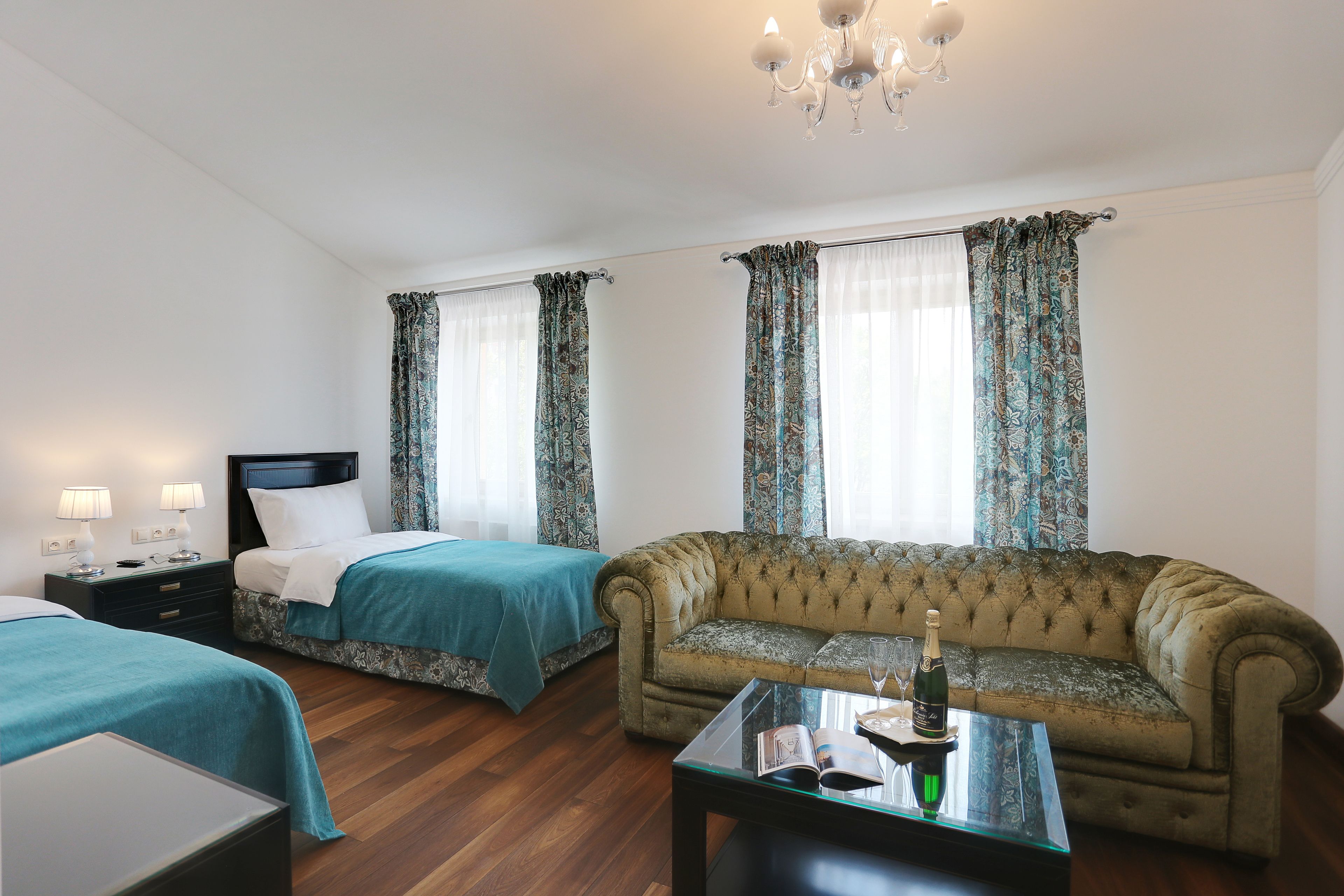A hotel room with two beds, a sofa, a glass coffee table, and a chandelier.