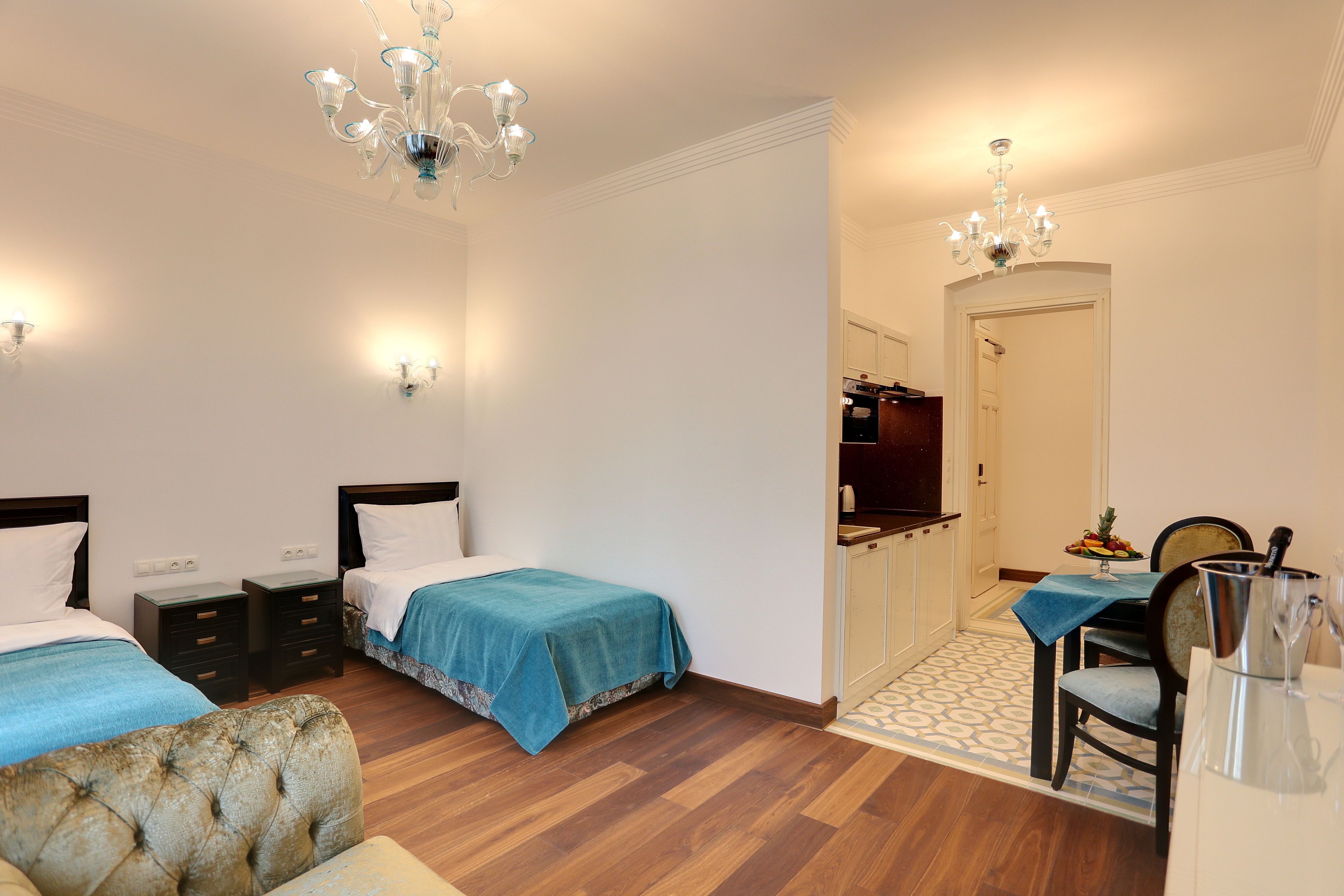 Une chambre avec deux lits, un lustre, des tables de chevet et un coin repas avec une table et des chaises.