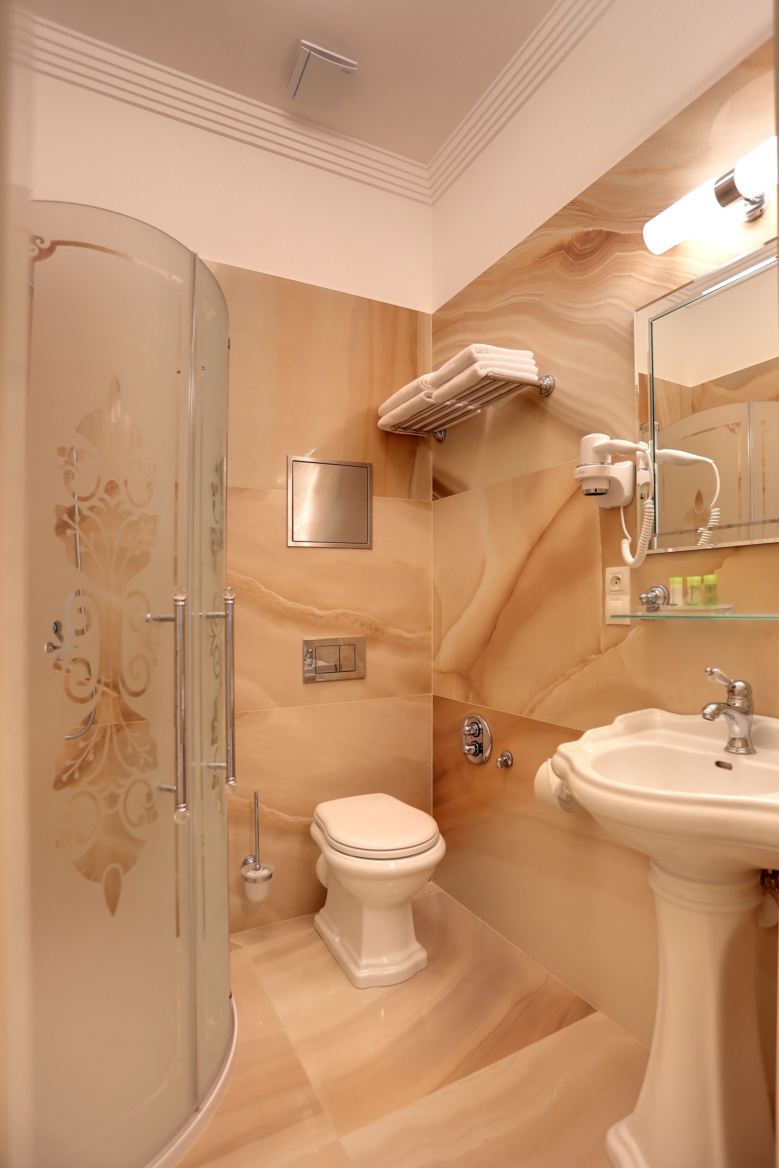 A bathroom with a glass shower enclosure, a toilet, a sink, and a hairdryer mounted on the wall.