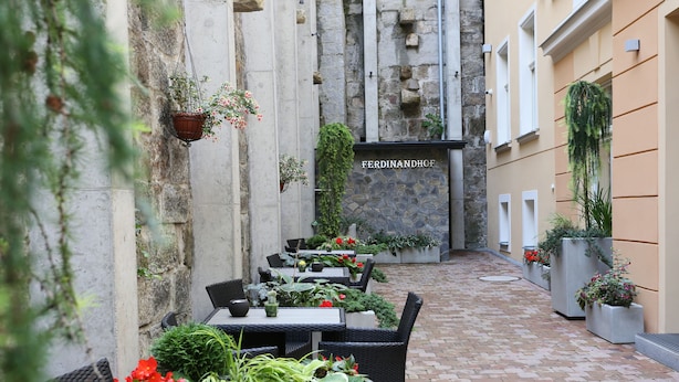 An outdoor seating area with wicker tables and chairs, surrounded by potted plants and a stone wall. - Ferdinandhof Apart-Hotel (Karlovy Vary)