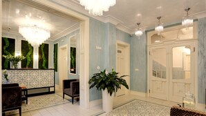 A spacious lobby with a patterned floor, a large potted plant, and a seating area with a patterned chair. - Ferdinandhof Apart-Hotel (Karlovy Vary)