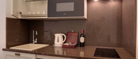 A compact kitchen with a microwave, kettle, and wine bottle.