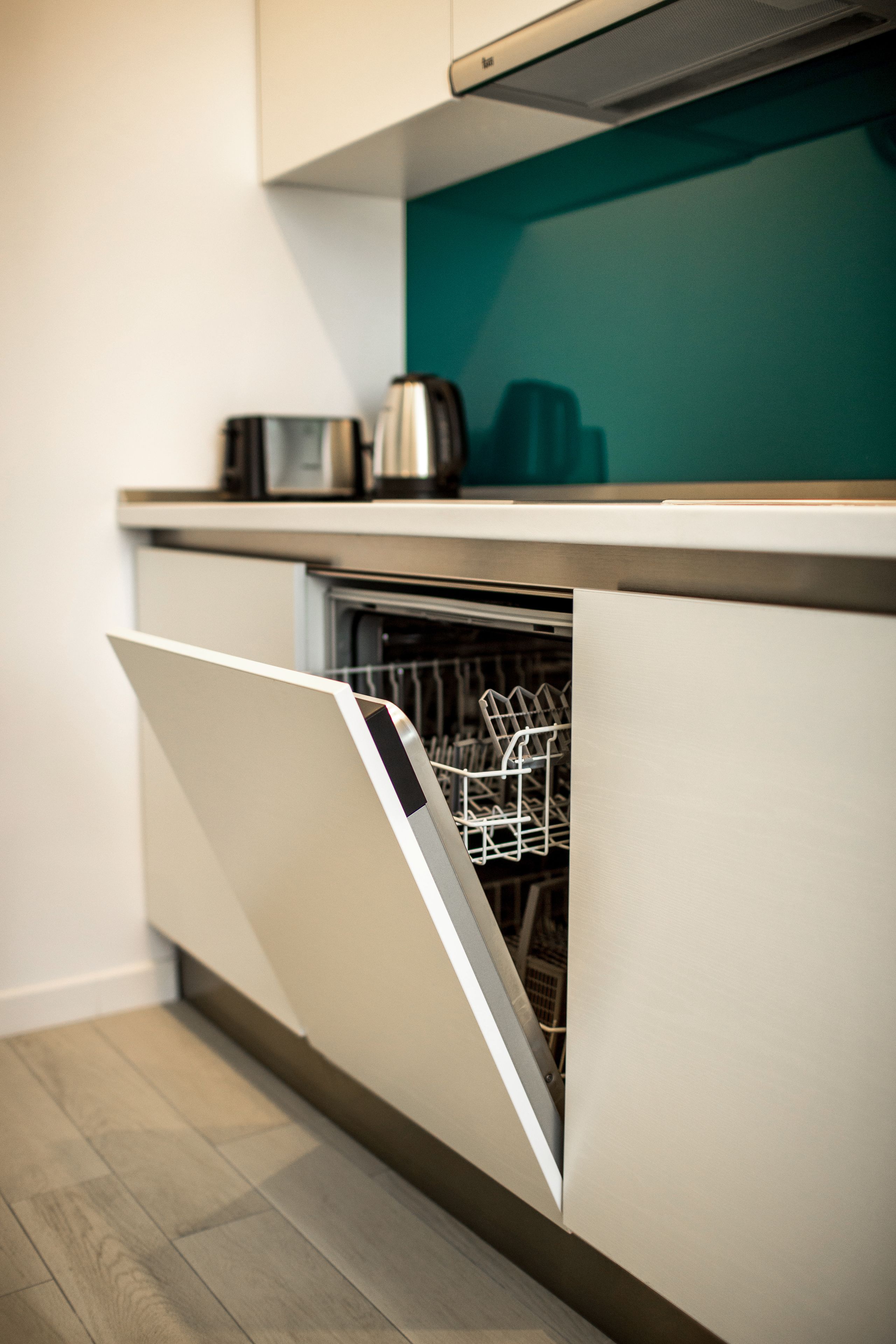A modern kitchen with a dishwasher, a microwave, and a kettle on the countertop.