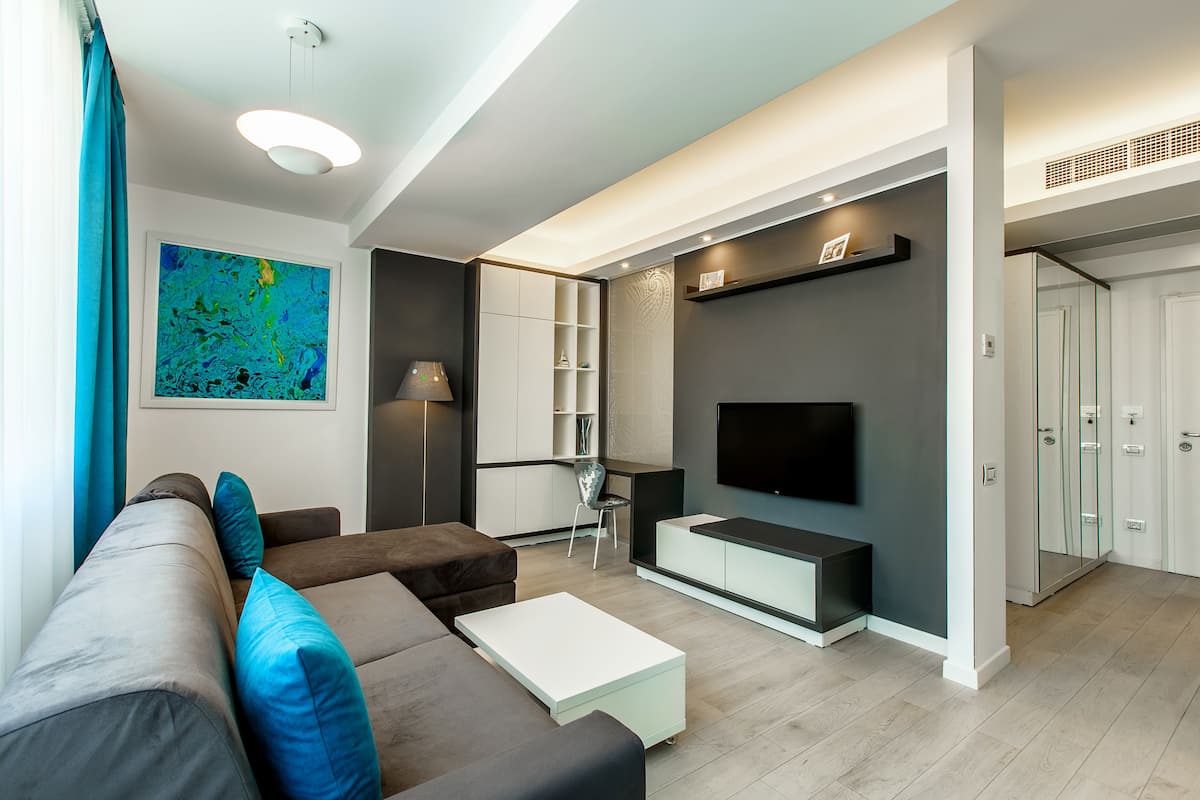 A modern living room with a sofa, coffee table, and TV. There is a small seating area with a chair and shelves.