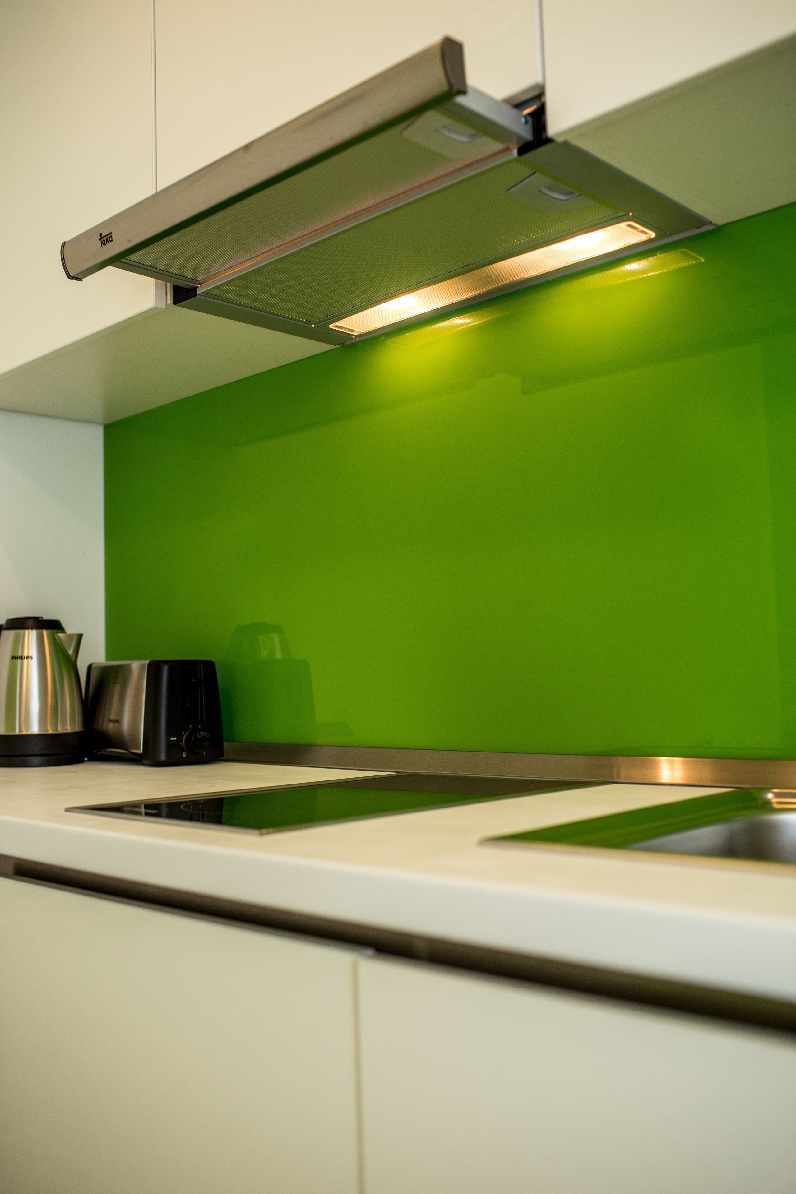 Une cuisine avec un plan de travail vert, une bouilloire en acier inoxydable, un grille-pain et un évier.