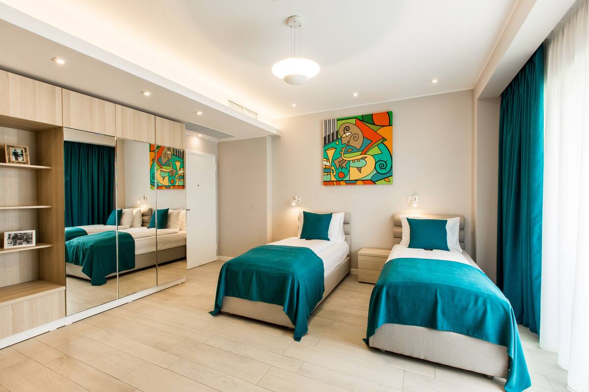 A modern bedroom with two beds, a large mirror, and a colorful abstract painting.