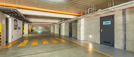 A clean, well-lit parking garage with concrete walls, yellow safety lines, and a blue door labeled "Hobby Room".