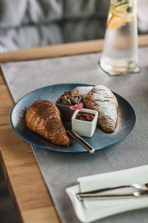 A plate with a croissant, a chocolate dessert, and a small bowl of jam on a blue plate.