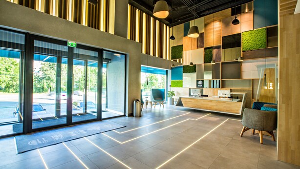 A modern reception area with a reception desk, seating, and large windows. - Mava Apartamente (Constanta)